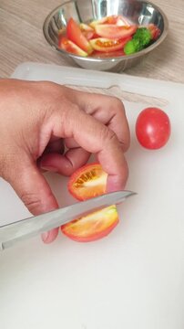 A person using a kitchen knife to slice fresh red tomatoes on a white cutting board for meal preparation