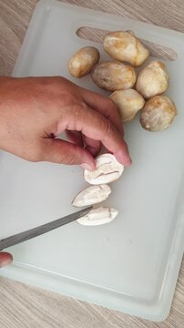A person using a kitchen knife to slice fresh straw mushrooms on a white cutting board for meal preparation