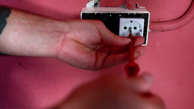 Electrician hand unscrewing electrical socket coverplate
