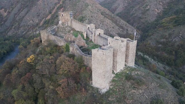 Pulling back aerial shot captures the ancient fortifications of Maglic fortress at twilight, surrounded by the dramatic landscape of Southwestern Serbia.