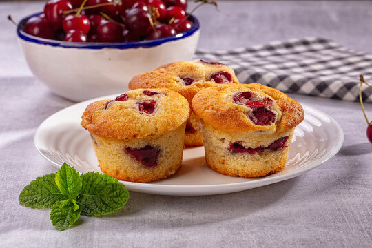 Cherry muffins on white plate with fresh mint and bowl of cherries