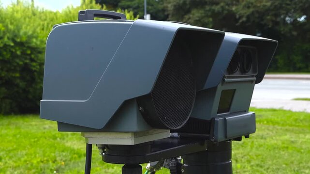 Mobile police speed enforcement camera system on a tripod next to the road measuring the velocity of passing traffic to detect speeding violations and issue fines for improved road safety