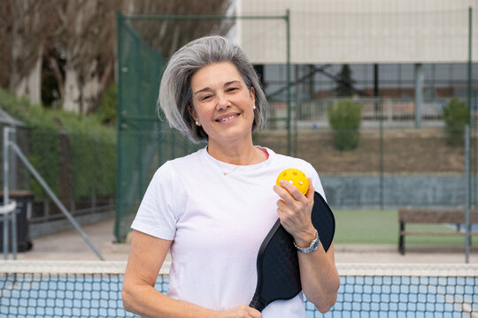 Senior woman enjoying active lifestyle, holding pickleball paddle and ball on court