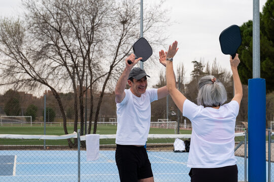 Happy senior couple celebrating a point playing pickleball on an outdoor court