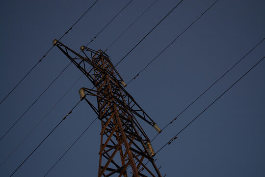 High voltage electric pylon against clear blue sky at sunset. Metal transmission tower with power lines for electrical energy supply and industry infrastructure grid distribution.