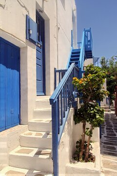 Narrow cobblestone street in Mykonos town with traditional whitewashed houses and vibrant pink bougainvillea flowers in full bloom. Picturesque Cycladic architecture featuring painted stone pavements 