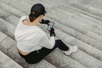 Obraz premium Young woman checking phone while seated on concrete stairs