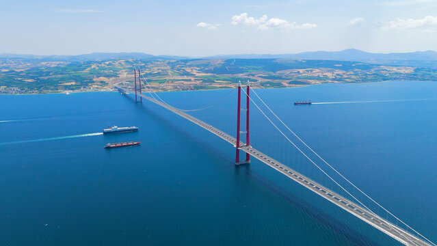Lapseki, Turkey. 1915 Canakkale Bridge with moving cars above and multiple cargo ships and a passenger ferry on the Dardanelles below. Aerial View