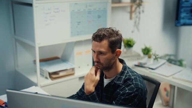 Young Caucasian male programmer writes code using multiple screens in home office workspace. AI development, cybersecurity, network database system, software engineering, remote tech startup concept.
