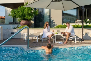 Couple Relaxing by Private Pool With Child Swimming While Working and Enjoying Drinks © .shock