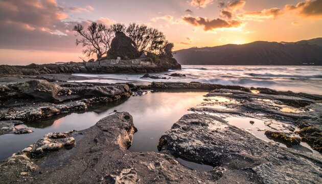 Dramatic sunset over a rugged coastline with rocky tide pools and a distant island rock formation