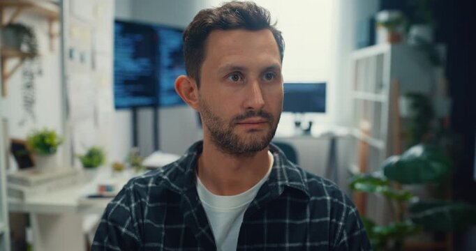 Young Caucasian male programmer writes code using multiple screens in home office workspace. AI development, cybersecurity, network database system, software engineering, remote tech startup concept.