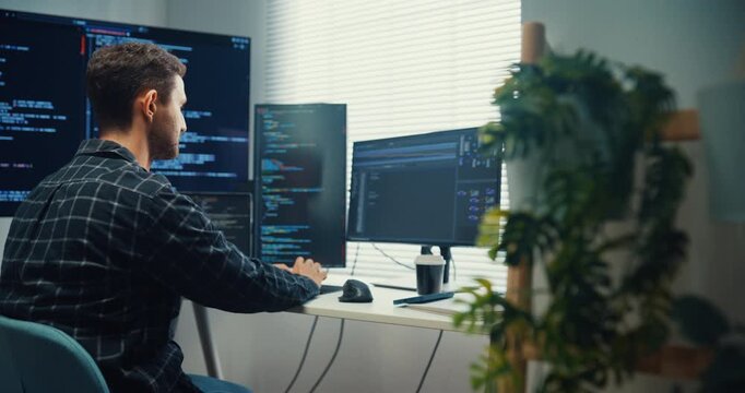 Young Caucasian male programmer writes code using multiple screens in home office workspace. AI development, cybersecurity, network database system, software engineering, remote tech startup concept.