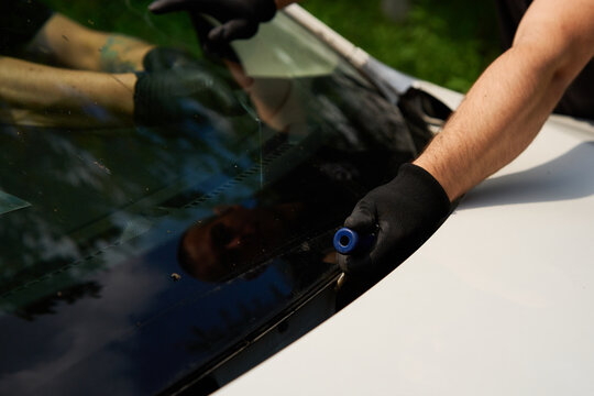 Automotive technician performs a car window extraction in a repair garage by skillfully pulling a cutting wire through the adhesive under the damaged glass