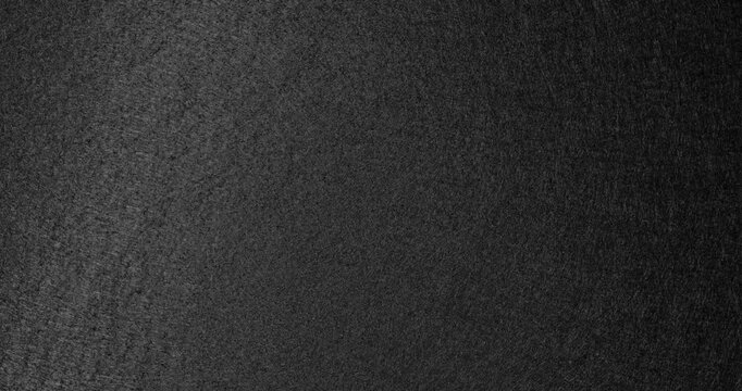 Rotating Black Rough Texture. Soft light moves across a grainy matte surface during smooth rotation, creating a dark abstract background.