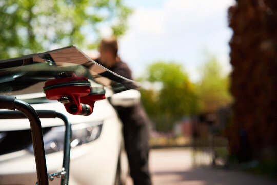 Red vacuum lifter holds new transparent car glass securely on an outdoor repair stand for mobile windshield replacement