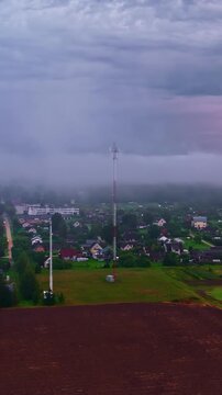 Foggy aerial perspective of a telecommunication mast and a small town under heavy clouds