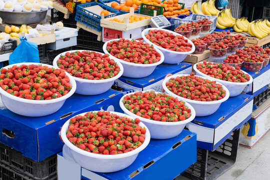 Fresh strawberries in white bowls displayed at an outdoor fruit market in Bukhara, Uzbekistan. Colorful bazaar stall with abundant seasonal berries, bananas, and oranges. Ideal for travel, food.