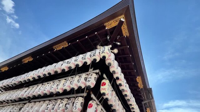 Upward view of ornate shrine roof with rows of Japanese lanterns against blue sky