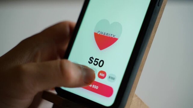 Hand holding smartphone with charity donation app showing donate button on screen 