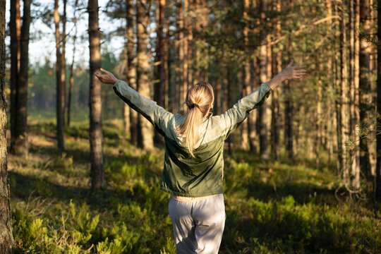 Woman stand in forest with outstretched hands emerging in nature and relaxation on recreational walk, female hiker exploring woodlands and practicing forest bathing for stress relief and wellbeing.