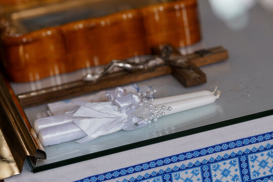Decorated white wedding candles with ribbons and pearls resting on glass near a wooden crucifix
