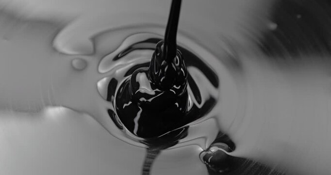 Black Viscous Liquid Pouring. Glossy fluid falls into a reflective pool, creating concentric ripples and swirling abstract forms.