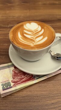 Small cup of cappuccino on Egyptian pound notes on wooden cafe table. Steam, warm light. Currency and coffee. Cozy very relaxing atmosphere of daily life!!