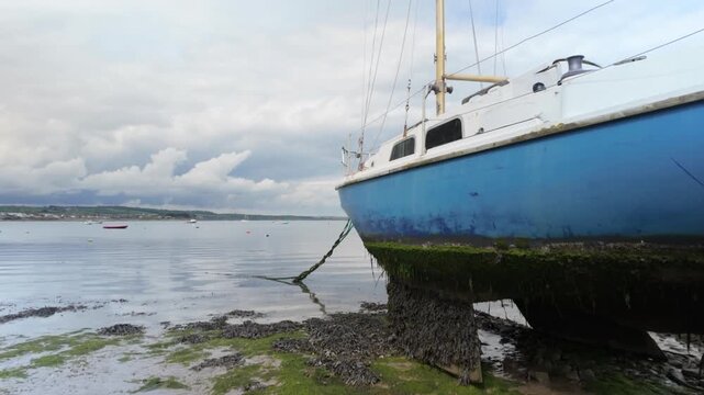 Sailboat resting on tidal mudflats at low tide with calm water and cloudy sky
