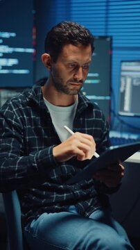 Vertical Screen : Young Caucasian male programmer use tablet for code design and plan in office at night. AI technology, cybersecurity, software developer, freelance innovation, digital data network.
