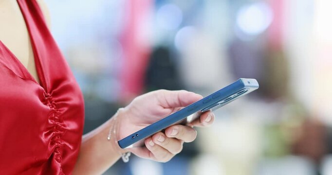 Woman using a smartphone while wearing a red blouse with colorful bokeh background. Mobile technology, communication, digital lifestyle, messaging, and connectivity, close-up