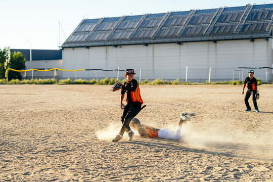 Young baseball players competing on a dusty dirt field, one sliding while defender attempts a tag out during a game