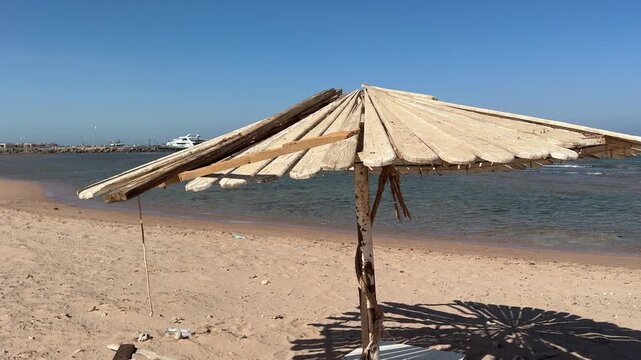 Old wooden plank sun umbrella on beach, weathered and tilted, rustic seaside shade, abandoned.