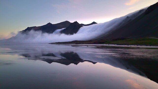 Misty Vestrahorn peaks emerging above fog bank with perfect water reflection, Stokksnes