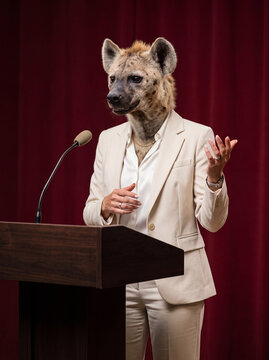 Speaker, politician or saleswoman, represented as a Hyena in beige suit behind lectern, gesturing. AI generated.