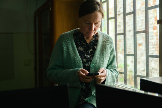 Woman using phone by the window of an old office library workspace, soft daylight and calm reflective atmosphere