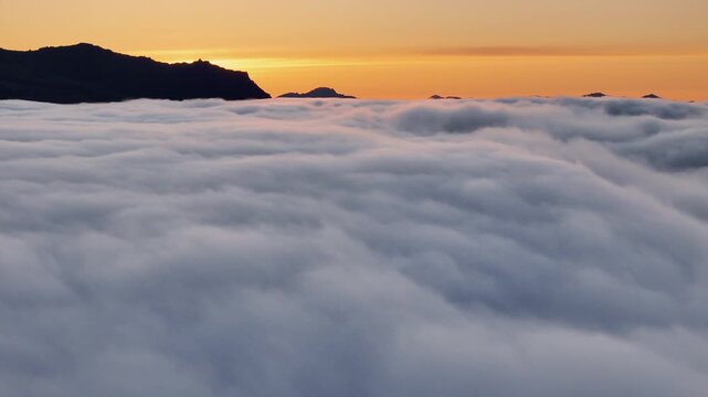 Steady hover above a dense cloud inversion as sunrise glows behind dark Austurland peaks, Iceland