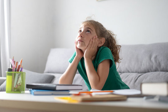 Thoughtful schoolgirl looking up while studying at home
