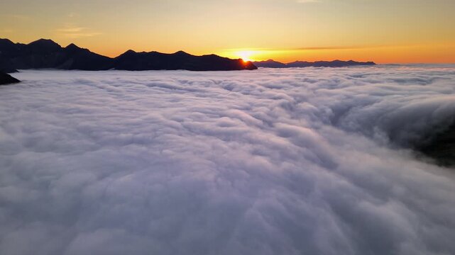 Low forward flight over the cloud inversion, heading into the sunrise glow between mountain peaks, East Iceland
