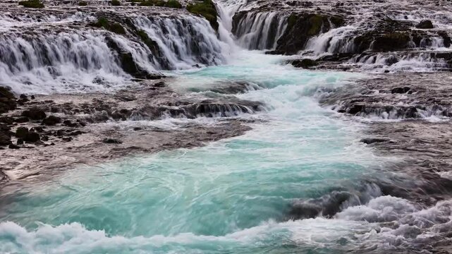 Low drone hovers over Bruarfoss turquoise pool and cascades mood shot for travel docs, South Iceland