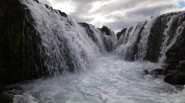 Hovering drone on Bruarfoss plunge under moody sky scene setter for travel docs, the Southern Region, Iceland