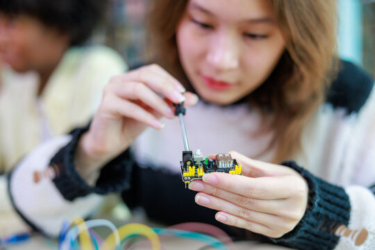 Selective focus on the hands of a happy teenage female student using a screwdriver to build a small electronic circuit board during a hands-on STEM education project.