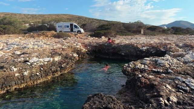 Joyful visitors swim in the crystal-clear waters surrounded by rugged rock formations on Paros Island. The sun shines brightly over this beautiful Cycladic paradise, perfect for relaxation.
