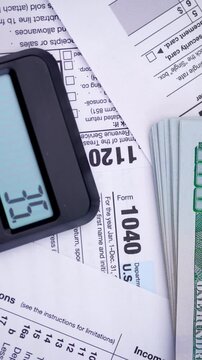 Calculating Income Tax Return. US Tax Forms with Cash. A calculator, red pen and dollar bills lie on income tax documents during a smooth close-up pan.