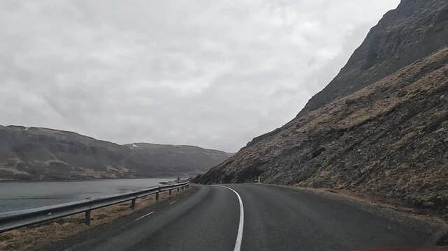 Route 47 winding along narrow Hvalfjordur fjord between steep basalt cliffs and water, West Iceland, Iceland