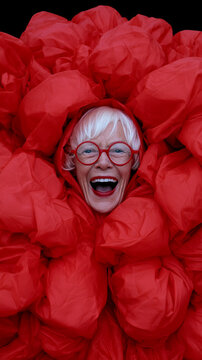 Senior woman laughing joyfully in bright red fabric. Elderly gentleman expressing happiness with vibrant red backdrop.