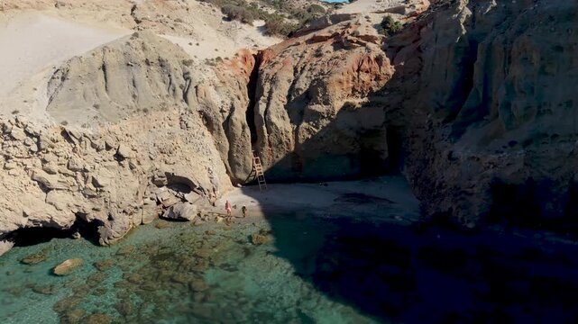 A couple of men and woman walks at the Tsigrado Beach. Milos Greece, where vibrant blue waters meet breathtaking cliffs. Experience tranquil moments at secret beaches surrounded by natural beauty