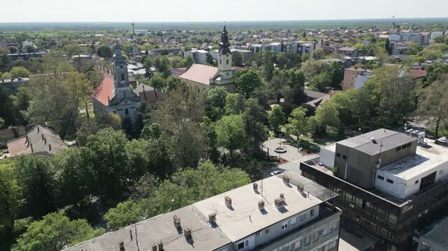 Aerial drone view gliding over the lush, tree-filled town of Vrbas on a sunny day in Northern Serbia.