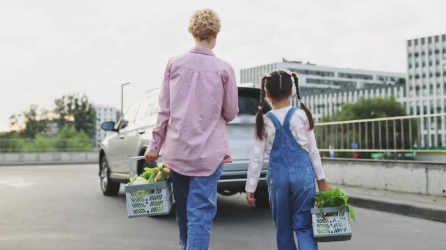 A Caucasian mother and her daughter are packing groceries into the trunk of a car after shopping