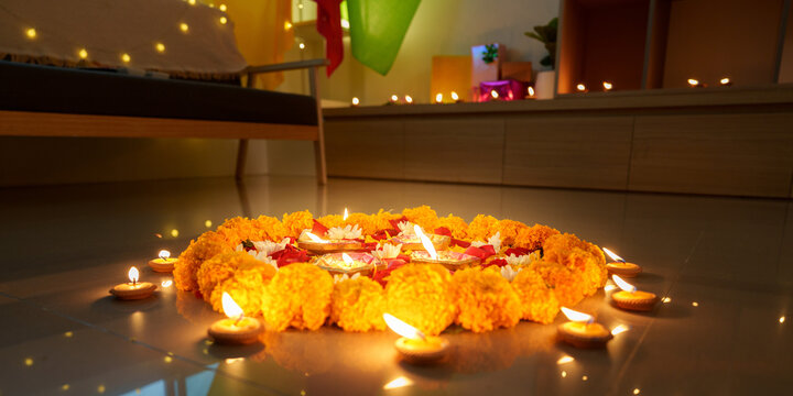 Flower rangoli with burning clay diyas on floor for Diwali celebration